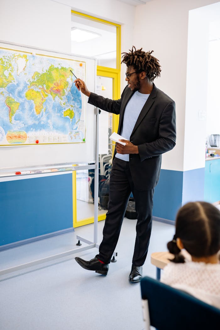 services-img-03 A male teacher explains world geography using a map to students in a classroom.